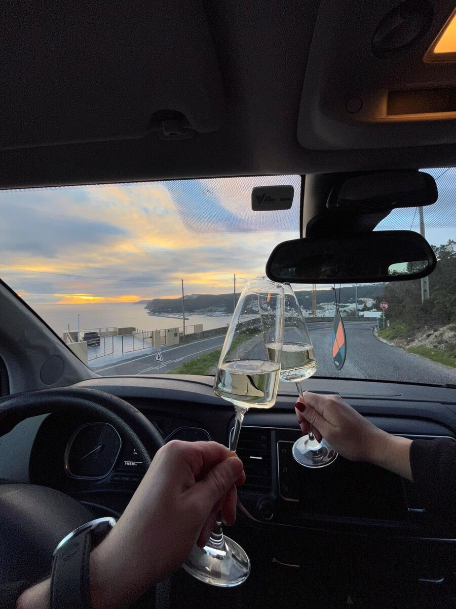 A toast with two glasses of white wine inside the van, overlooking the bay at sunset