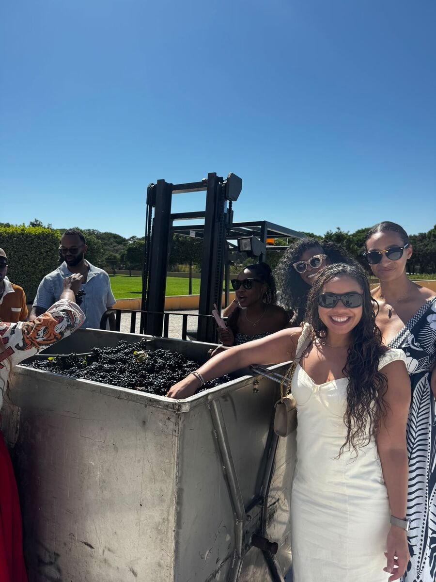 Guests smiling beside a steel tank of freshly harvested grapes during the harvest